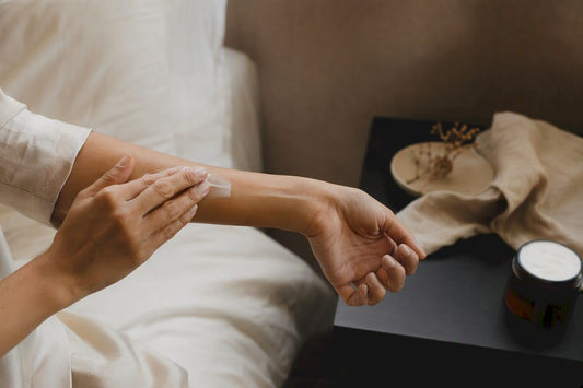 Hands scooping body butter onto forearm skin