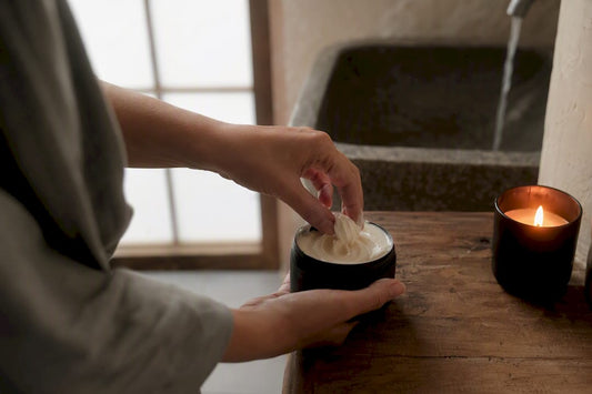 Hands scooping body butter with oil bottle